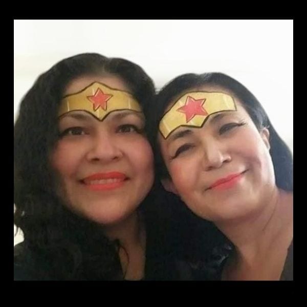 Two smiling women with Wonder Woman's gold tiara and red star painted on their foreheads