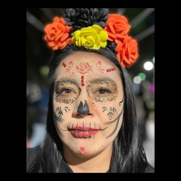 Woman with soft-toned Catrina makeup and a crown of orange and yellow roses