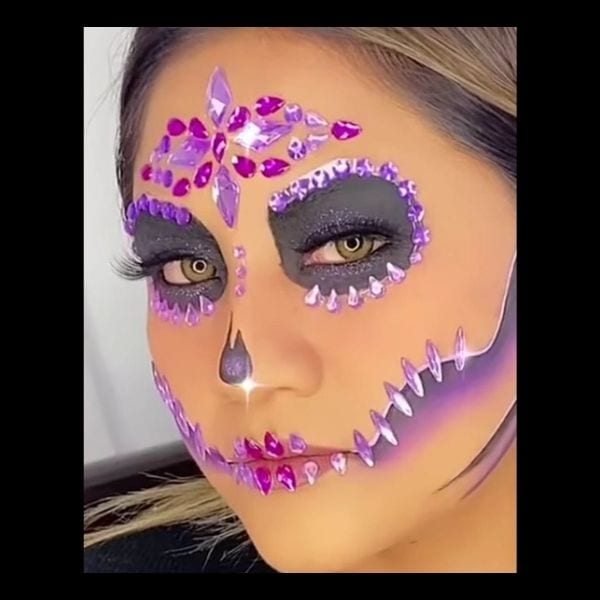 Woman with glam Catrina makeup featuring purple gems around the eyes, forehead and mouth
