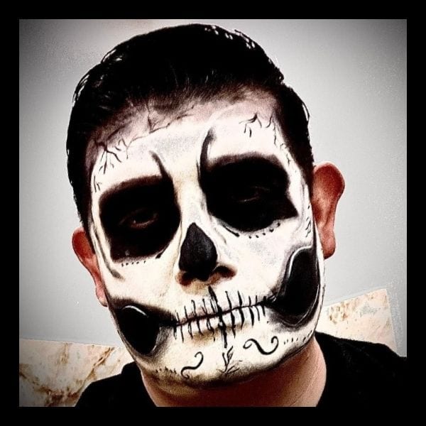 Man wearing classic skull makeup: white face, black eye sockets and nose, and drawn-on teeth
